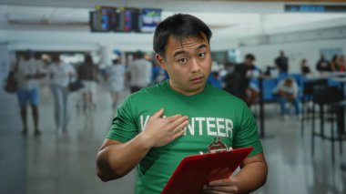 Kalabalık bir havaalanı terminalinde elinde bir pano tutan yeşil gömlekli genç adam arkasında bulanık gezginler olan bir iç mekanda örgütsel bir sahne sunuyor..