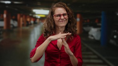 Kapalı otoparkta mola veren genç, kıvırcık saçlı ve gözlüklü bir kadın..