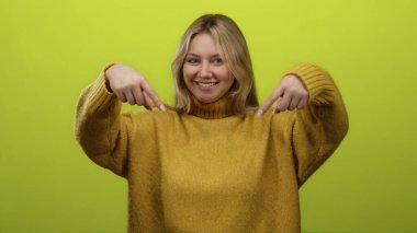 Hardal rengi süveter giyen, canlı yeşil arka planda gülümseyen, neşe ve pozitiflik saçan, elleri neşeyle aşağıya bakan, parlak bir stüdyoda yakalanmış bir kadın..