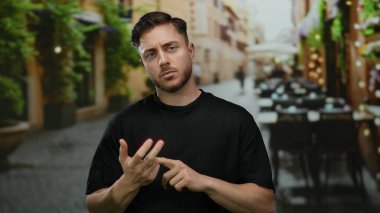 Sakallı genç adam bir şehir restoranının terasında parmaklarını sayıyor. Etrafı bitki ve sandalyelerle çevrili..