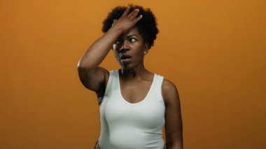 Alnı turuncu arka planda duygularını ifade eden beyaz kolsuz bluz giyen bir kadın çeşitli sözlü olmayan iletişim hareketleri sergiliyor..