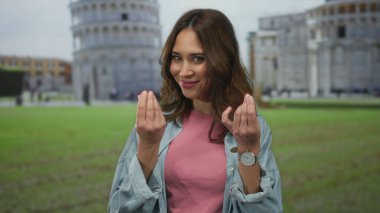 İspanyol kadın, Avrupa 'nın ünlü bir şehir simgesi olan Pisa, İtalya' daki ikonik eğik kulenin önünde para jesti yapıyor..