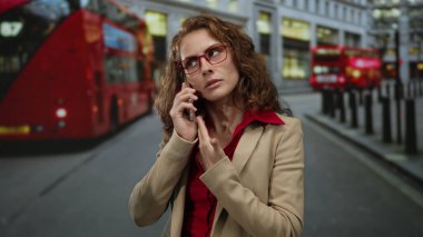 Şehir caddesinde akıllı telefondan konuşan bir kadın yoğun bir şehir ortamından geçen çift katlı otobüslerle modernlik ve geleneğin bir karışımını sergiliyor..