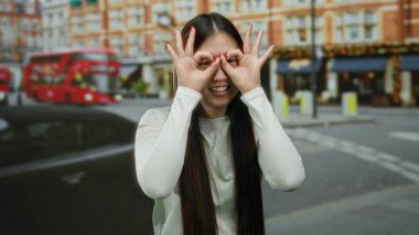 Arka planda ikonik kırmızı otobüslerle gülümseyen kadın şehir ortamında neşeli bir ifade ve neşe sergiliyor.