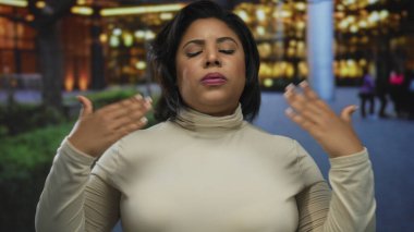 İspanyol kadın şehir caddesinde gözleri kapalı ve ellerini kaldırarak duruyor, akşam kent ortamında duyguları yansıtıyor ve arka planda aydınlık binalar var..