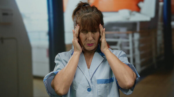 Hispanic senior woman cleaner appearing stressed while on a cruise ship deck, wearing a uniform and standing amidst sunny outdoor maritime surroundings.