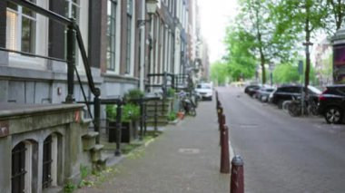 Tuğla binalar, park edilmiş bisikletler, arabalar ve yeşil ağaçlarla Amsterdam 'daki sönük sokak manzarası sakin bir şehir manzarası yaratıyor..