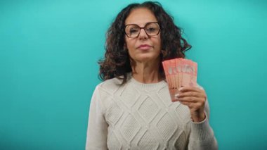 Orta yaşlı bir kadın elinde mavi arka planda Malezya bankaları tutuyor, gülümsüyor ve gururla kendisine işaret ediyor..