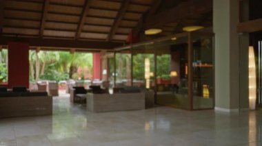 Lüks bir otel lobisinin kapalı görüşü. Parlak güneşli bir günde tropikal bahçeli modern koltuklar..