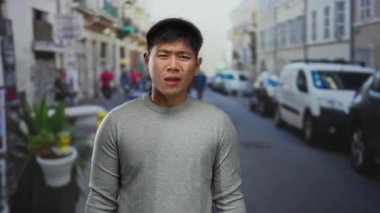 Sokaktaki genç adam, arka planda trafik ve yayaların görüldüğü hareketli bir şehir sahnesinde kargaşa yaratıyor.