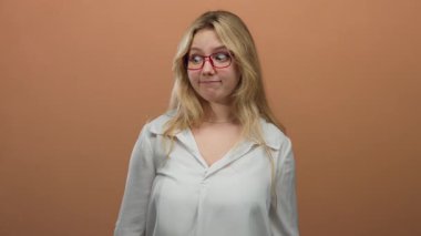 Mizahi bir şekilde, geniş gözlü, kırmızı gözlüklü ve koyu kahverengi arka planda beyaz bluzlu bir deli gibi hareket eden bir kadın..