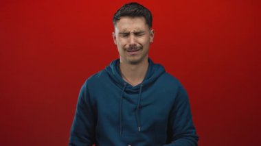 Mavi kapüşonlu genç adam sıkıntılı ve duygusal bir şekilde kırmızı bir arkaplanda beliriyor. Üzüntü ve içgözlem hissini gözleri kapalı aktarıyor..