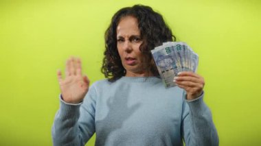 Orta yaşlı bir kadın, Güney Afrika banknotlarını açık sarı bir zemin üzerinde tutan endişe ifadeleri mali kararları veya bolluğu akla getiriyor.