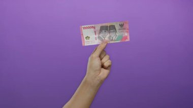 Endonezya Rupiah banknotunu elinde tutan adamın eli mor renkli bir arka planda, izole bir şekilde para ve ekonomi sergiliyor..