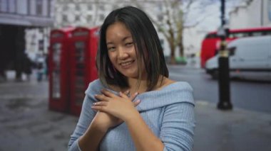 Hareketli bir şehir caddesinde ikonik kırmızı telefon kulübeleriyle gülümseyen bir kadın canlı bir şehir manzarası yakalıyor..