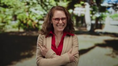 Kırmızı gözlüklü genç bir kadın, güneşli bir parkta, etrafı yemyeşil bir zemin ile çevrili, heyecan ve pozitifliğini ifade ediyor..