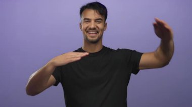 Genç İspanyol bir adam, neşeli ve yaratıcı bir stüdyo ortamında izole edilmiş mor bir arka plana karşı elleri ile bir çerçeve hareketi yaparken gülümsüyor..