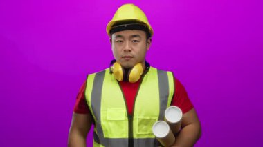 İnşaat malzemesi giyen Asyalı genç bir adam, elinde parlak pembe bir arkaplan planı tutarken öpüşüyor. Oyuncu ama profesyonel bir mimari tema sergiliyor..