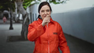 Turuncu hapisteki kadın sokakta jest yapıyor, arka planda ağaçlar ve duvarlar olan neşeli duygular ifade ediyor, özgürlük ve mizah gösterisi yapıyor..