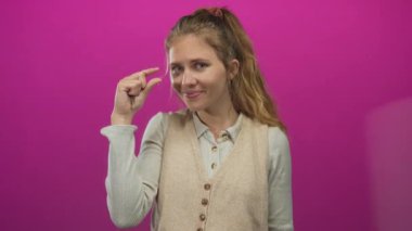 Kadın, sarı saçlı süveter tasarımını ön plana çıkarmak için genç ve etkileyici bir sarışının olduğu bir stüdyoda parmak çimdikleme hareketi yapıyor..