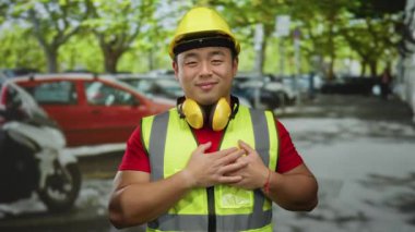 Kasklı gülümseyen adam güneşli bir günde arka planda arabaları olan kalabalık bir şehir sokağında şükranlarını sunuyor.