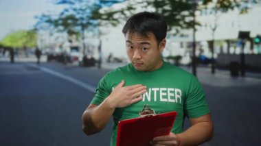 Şehir sokağında kırmızı pano ve yeşil gömlekli gönüllü bir adam açık gökyüzü altında dalgın dalgın dalgın bir şekilde duruyor.