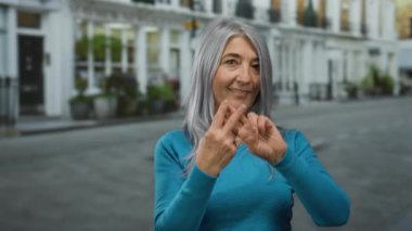 Üst düzey bir kadın, şehir kültürünün ve sosyal etkileşimin samimi bir anını yakalamak için şehir sokaklarında mavi bir kazak giyip hashtag jesti yapıyor.