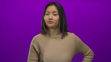 Genç bir kadın, canlı mor bir arkaplan karşısında iki parmağıyla ihtiyatlı bir jest yapar. Farkındalık ve odaklanma duygusunu aktarır..