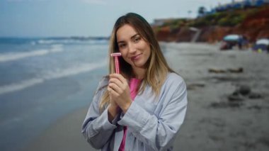 Güneşli bir günde elinde jiletle gülümseyen bir kadın canlı bir deniz arka planına sahip neşeli açık hava aktiviteleri sergiliyor..