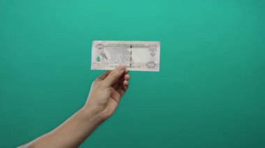 Yeşil arka planda 500 dirhem birleşik Arap Emirliği banknotunu elinde tutan bir adamın eli, izole bir ortamda para ve finansman gösteriyor..