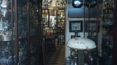 İçinde çeşitli seramiklerle dolu cam dolaplar ve ön planda bulanık eski bir lamba bulunan loş antika mağazasının iç manzarası..
