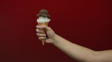 Dondurma külahını canlı kırmızı arka planda tutan adam ikramlara ve ellere odaklanmak için zıtlık ve dokuyu vurguluyor..