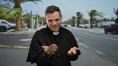 Siyah bornoz giymiş bir adam arka planda avuç içleriyle şehir sokağında duruyor. Duygularını gözler kapalı ve eller yüze yakın gösteriyor..