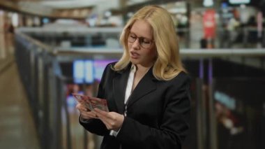 Alışveriş merkezinde yeni Zelanda doları sayan kadın sarı saç, alışveriş ortamı ve iş kıyafetleri, finansal başarı ve perakende heyecanı taşıyor..