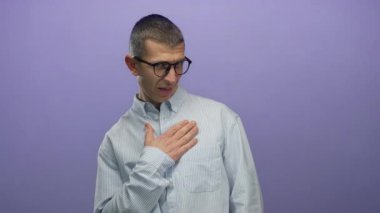 Gözlüklü ve çizgili tişörtlü bir adam göğsünde mor bir arkaplan ile poz veriyor..