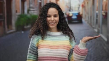 Kıvırcık saçlı, renkli kazaklı, gülümseyen ve şehir dışında bir sokakta el kol hareketi yapan, hoş bir tavırla hareketli bir şehir hayatı yaşayan bir kadın..