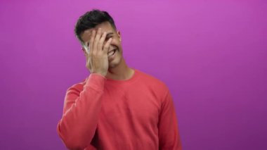 Kırmızı gömlekli genç adam canlı pembe bir arka plana gülümsüyor, neşeli ve arkadaş canlısı bir duruş sergiliyor..