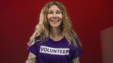 Kadın, kırmızı arka planda gülümseyen sarışın genç bir gönüllüyle göz makyajı yapıyor..