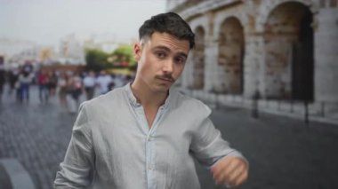 Kısa saçlı genç adam İtalya 'daki tarihi Roma Kolezyumu' nun yakınında dikiliyor ve arka planda turistlerin olduğu sıradan bir anı yakalıyor..