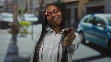 Güneşli şehir caddesinde, gözlüklü, çizgili tişörtlü, neşeli gülümsemeli ve rahat tavırlı bir şekilde el sıkışan bir kadın..