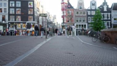 Amsterdam, Hollanda 'daki bulanık şehir manzarasında arka planda klasik kanal evleriyle kaldırım taşı caddesinde yürüyen insanlar vardı..