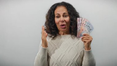 Tayland banknotlarını elinde tutan kadın, izole edilmiş beyaz bir arkaplan karşısında şaşırmış bir ifadeyle para ve duygu gösterisi yapıyor..