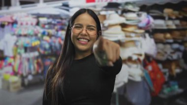 Canlı bir açık hava pazarında, renkli şapkalar ve sokak tezgahlarıyla çevrili gülümseyen gözlüklü kadın canlı bir Latin sokak görüntüsü yakalıyor..