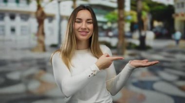 Şehirli bir sokak arkaplanında gülümseyen ve boş bir eli işaret eden bir kadın, açık havada beyaz kazaklı genç bir sarışının yer aldığı, canlı bir cazibeyle dolu..