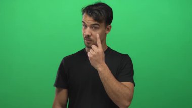 Siyah gömlekli genç İspanyol adam yeşil arka planda tetikte. Ciddi bir yüz ifadesi sergiliyor.