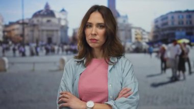 Vatikan 'ın San Pedro Meydanı' nda silahlı bir kadın dikiliyor. Bulanık tarihi binalar ve insanlar olan açık şehir manzarasını, pembe bir gömlekle sergiliyor..