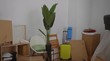Oturma odasında içi bitki ve bavul gibi taşınan eşyalarla dolu bir kutu taşıyan bir adam yeni bir ev kurulumunu öneriyor.