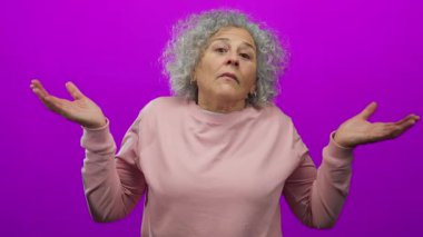 Gri saçlı, pembe kazaklı, elleri parlak pembe duvarlı bir kadın, kafa karışıklığı ya da belirsizliği ifade eder..