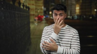 Kilisedeki genç adam şaşırmış görünüyor. Yüzünde çizgili tişört, kilisenin iç kısımları bulanık..