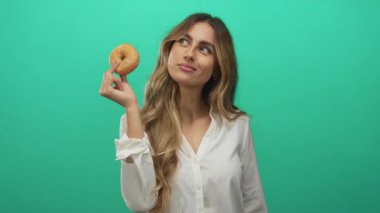 Stüdyoda genç sarışın kadın yüzüne jöleli donut tutar; cazibe merakı oyun düşkünlüğü.